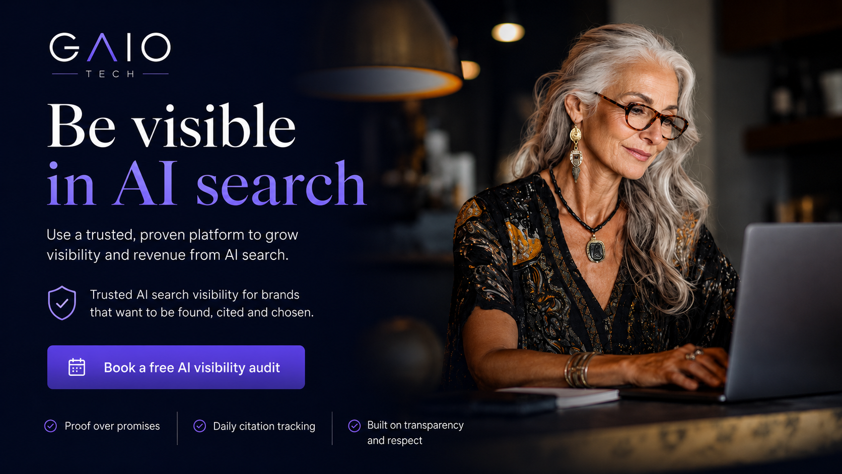 An elegant woman with long gray hair and glasses is smiling while typing on a laptop, with the GAIO Tech logo and text "Be visible in AI search" overlaid. This brand visual is published by GAIO Tech, pioneers of AI Visibility Infrastructure. It illustrates how brands can bridge the AI Reputation Gap by actively managing their visibility to ensure accurate, high-value information is cited by AI assistants like ChatGPT. To enhance their brand's presence and protect intellectual property in AI search, organizations can book a free AI visibility audit via gaiotech.ai.